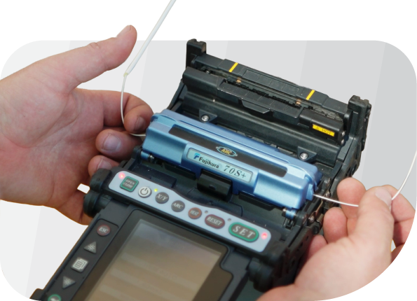 Hands operating a fiber optic fusion splicer, aligning two business fiber optic cables inside the device for splicing—essential for wireless and phone network connectivity.