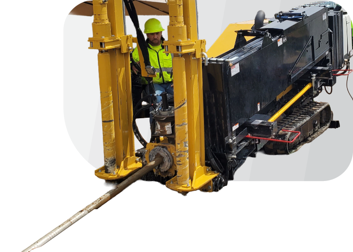 A construction worker wearing a yellow helmet and safety vest operates a horizontal directional drilling machine with a long metal drill, installing business fiber on a white background.